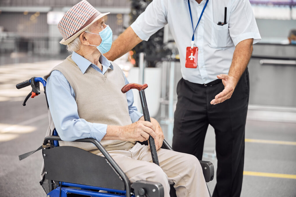 A man in a wheelchair with a cane and wearing a mask.